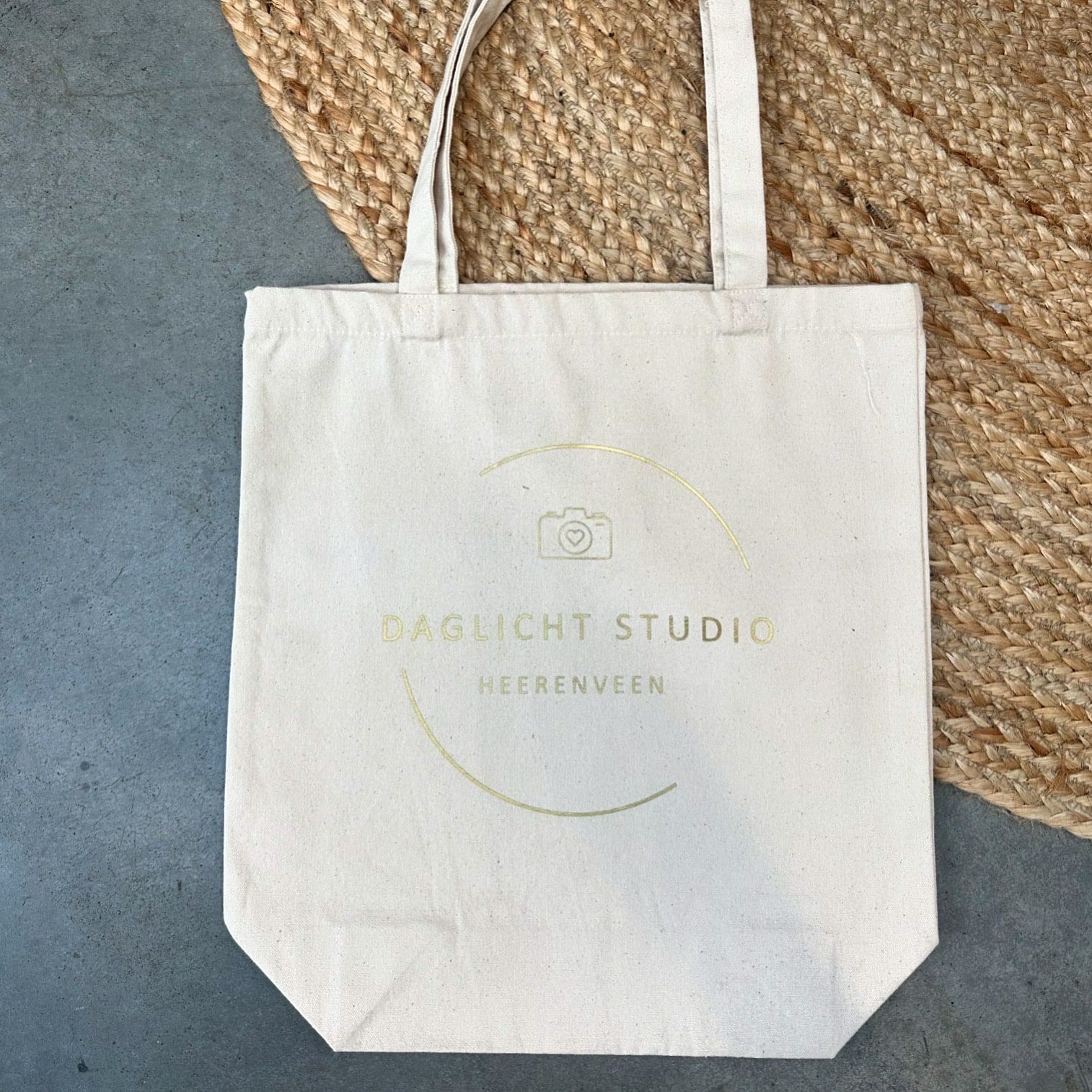 Canvas tas met het goudkleurige Daglicht Studio-logo op een gevlochten kleed