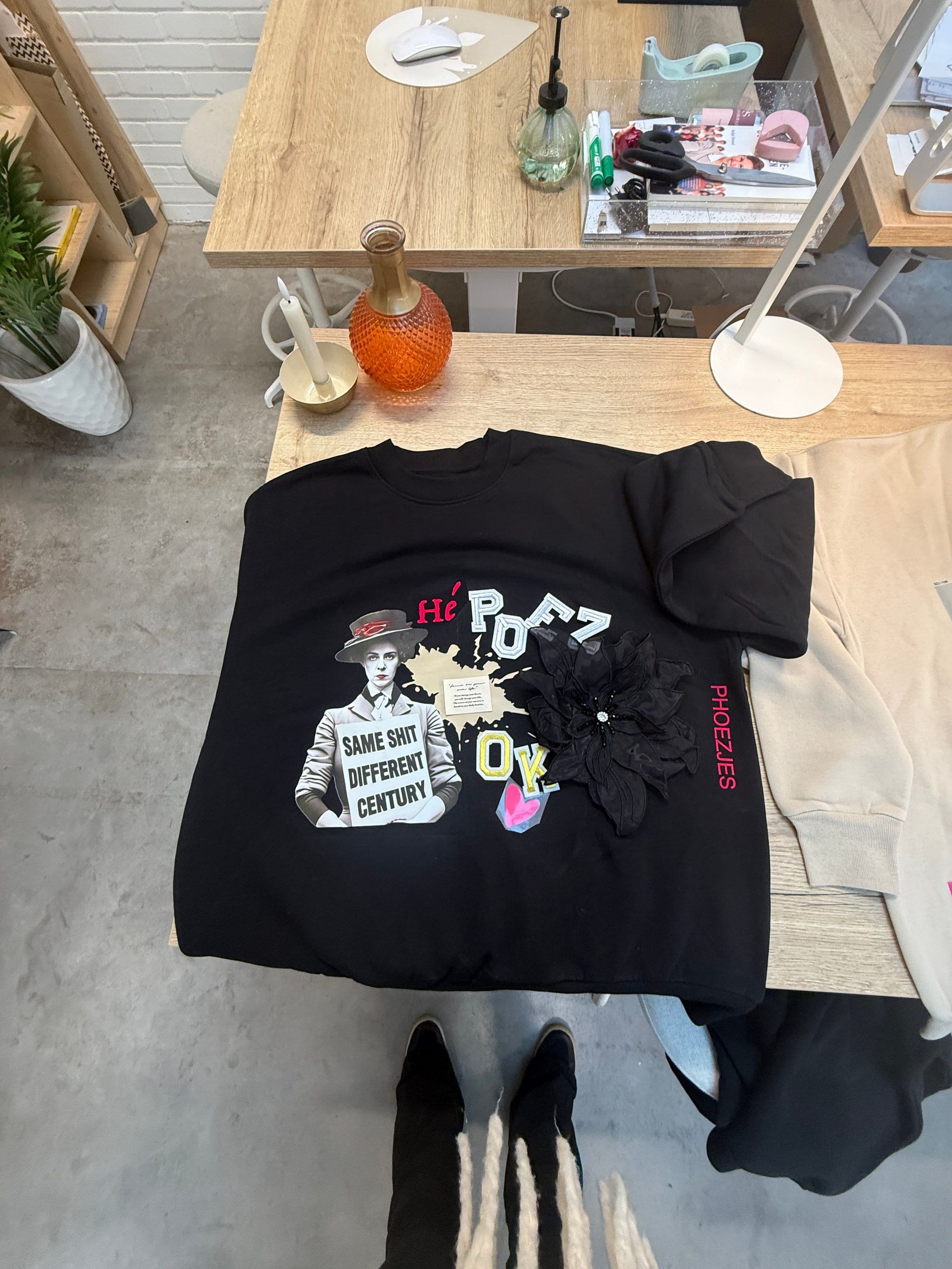 Zwarte PHOEZJES-sweater met collage-opdruk en stoffen bloem-applicatie op de werktafel