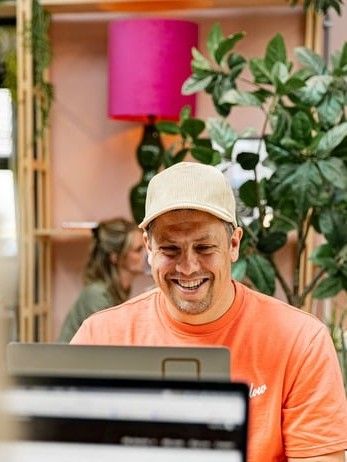 Thijs met pet, lachend achter zijn laptop